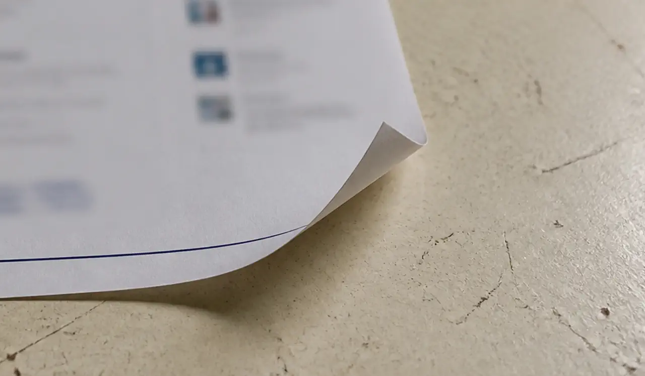 Laser-printed webpage on a worn desk, curled corner and a navy rule. The print stays blurred.